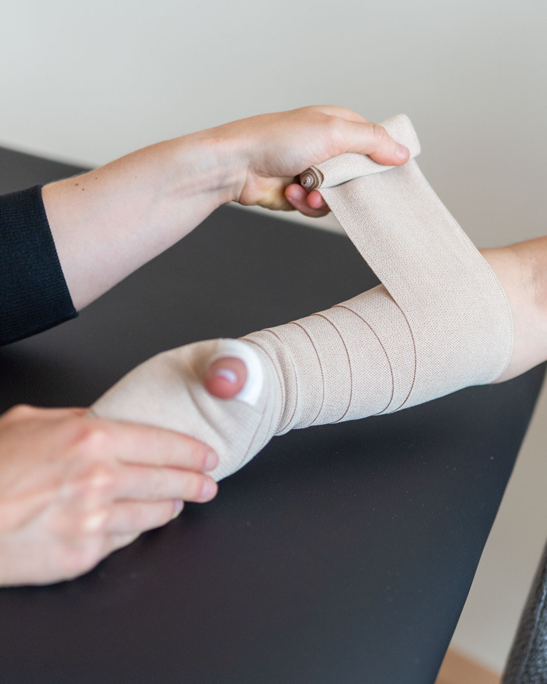 Das Bild zeigt eine Therapeutin, die sorgfältig einen Kompressionsverband am Arm eines Patienten anlegt – ein zentraler Bestandteil der Manuellen Lymphdrainage. Diese Behandlung unterstützt den Lymphfluss, reduziert Schwellungen und fördert die Heilung nach Operationen oder bei Lymphödemen. Die präzise Wickeltechnik ist entscheidend für eine effektive und angenehme Therapie.